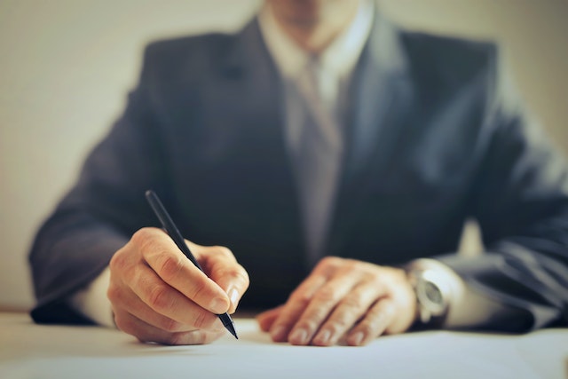 person in a suit using a black pen to sign a contract